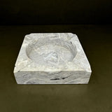 Marble square bowl with circular depression on a dark background